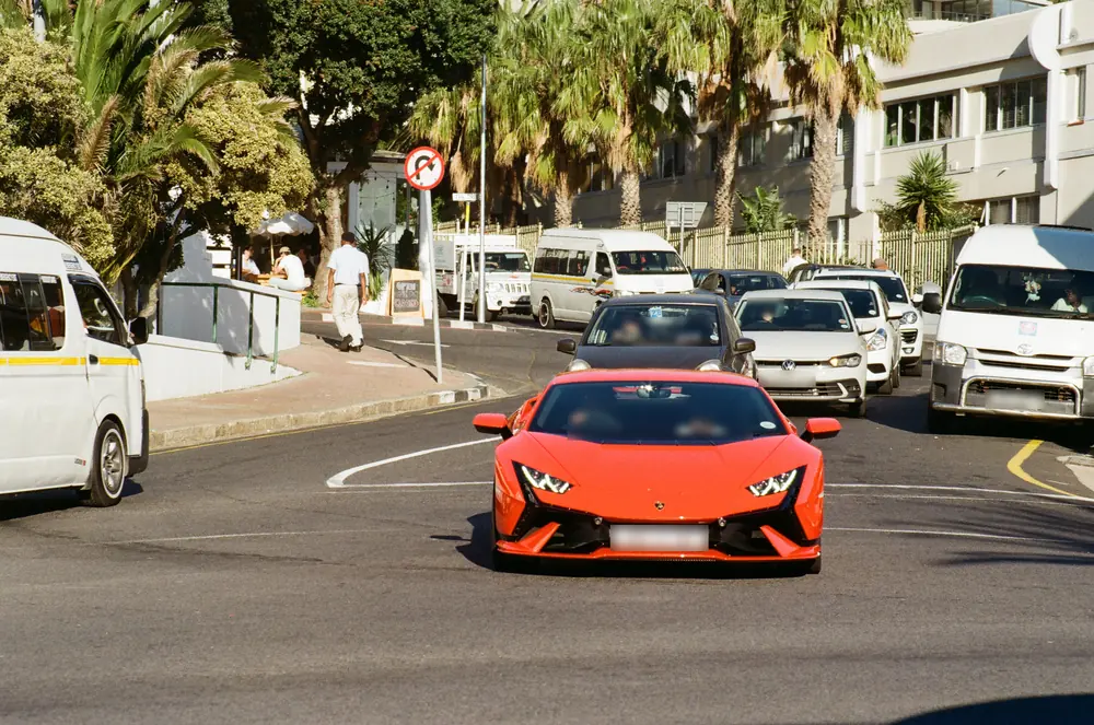 An orange supercar in Camps Bay traffic, plates blurred